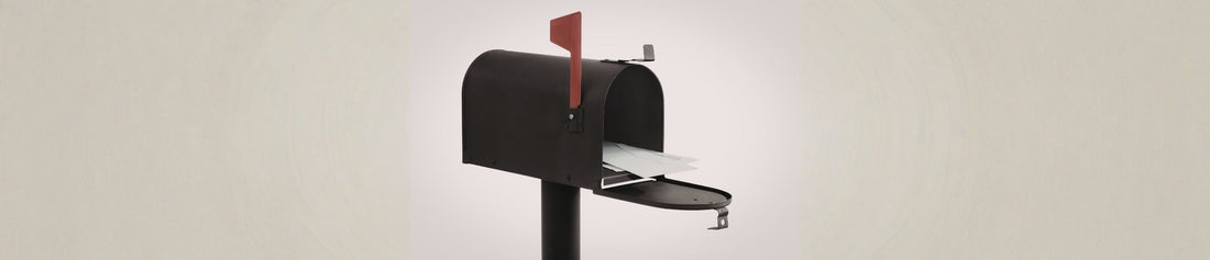 An open black metal mailbox on a post against a plain, neutral-toned background.