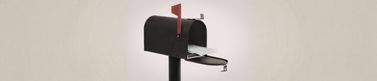 An open black metal mailbox on a post against a plain, neutral-toned background.