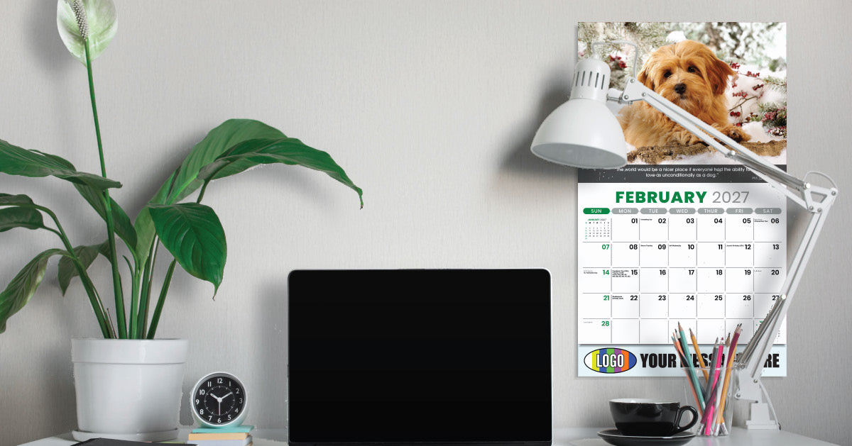 Desk setup with a laptop, calendar, lamp, and plant on a light gray wall background.