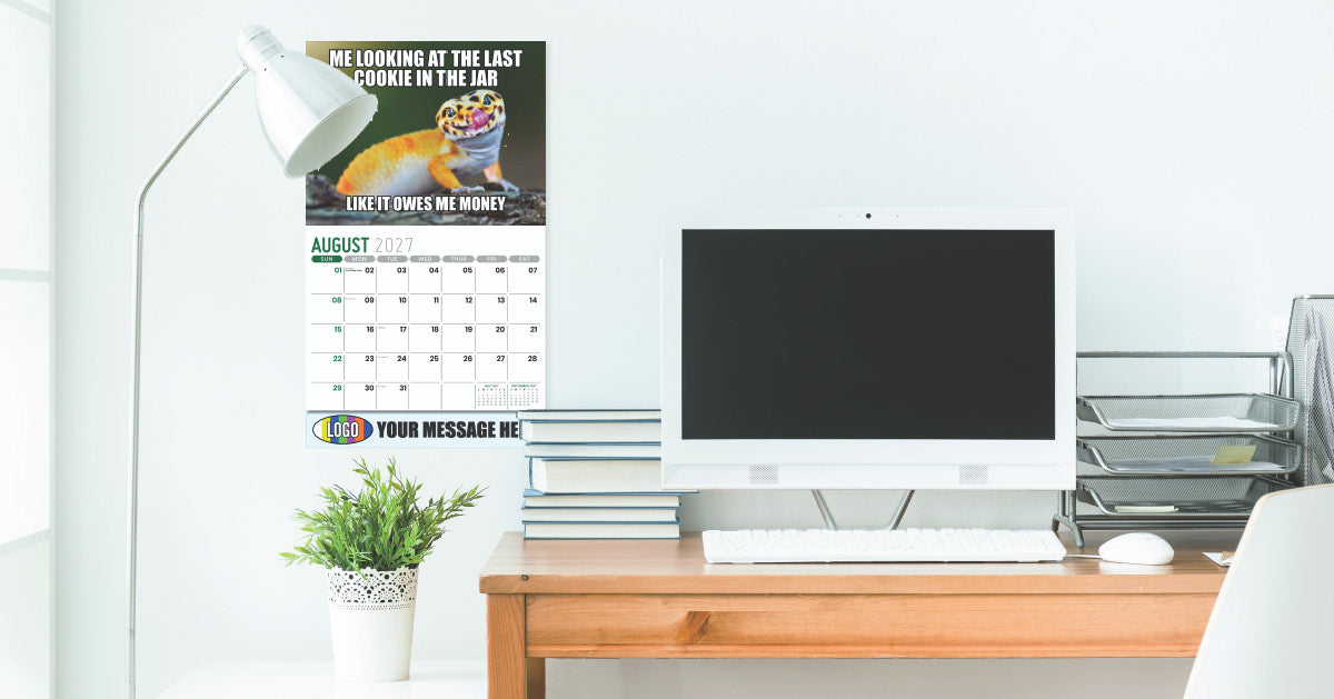 Branded wall calendar on plain wall with computer desk, plant and lamp